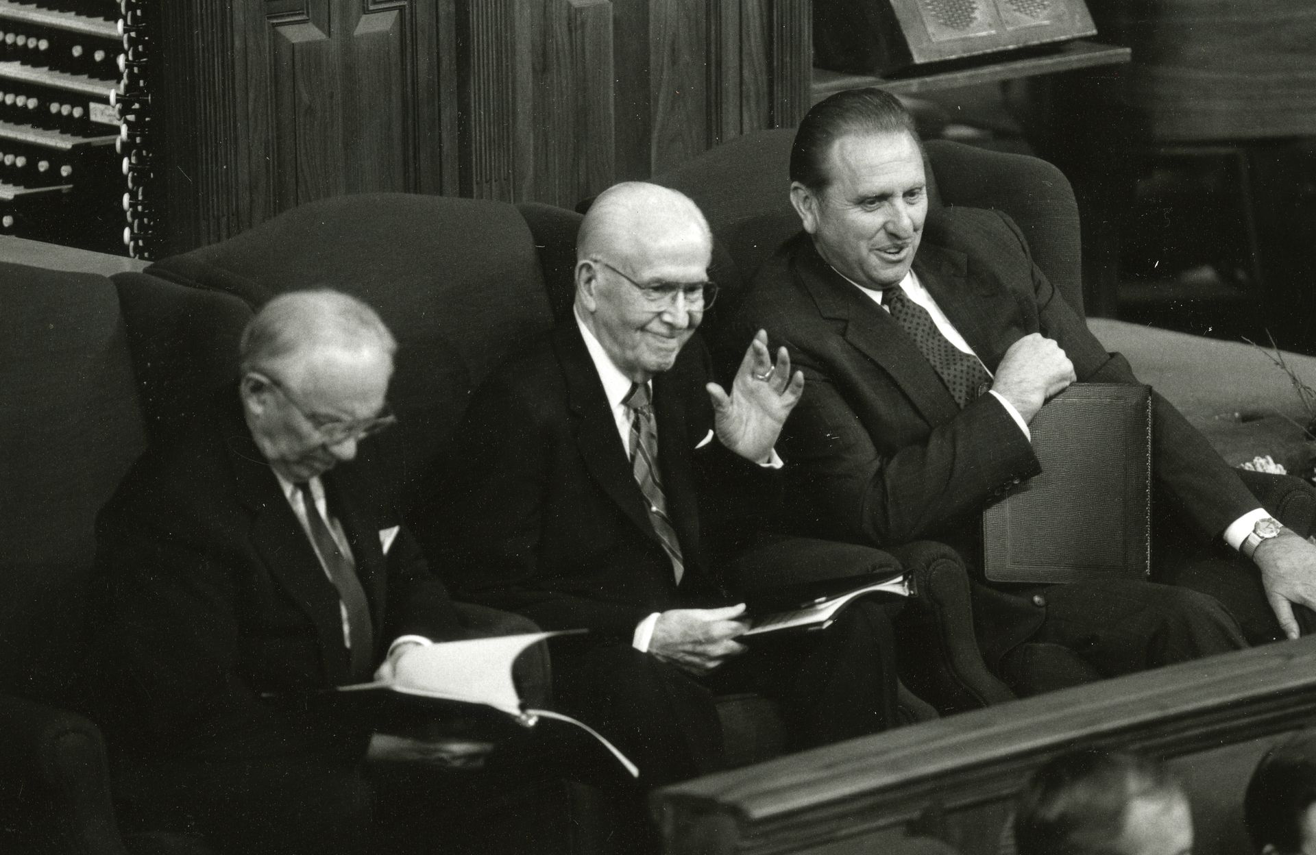 President Benson sitting between his counselors and waving to the audience in the Tabernacle.