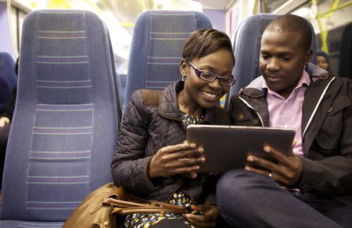 Couple sitting together on a bus.  They are looking at a tablet computer.