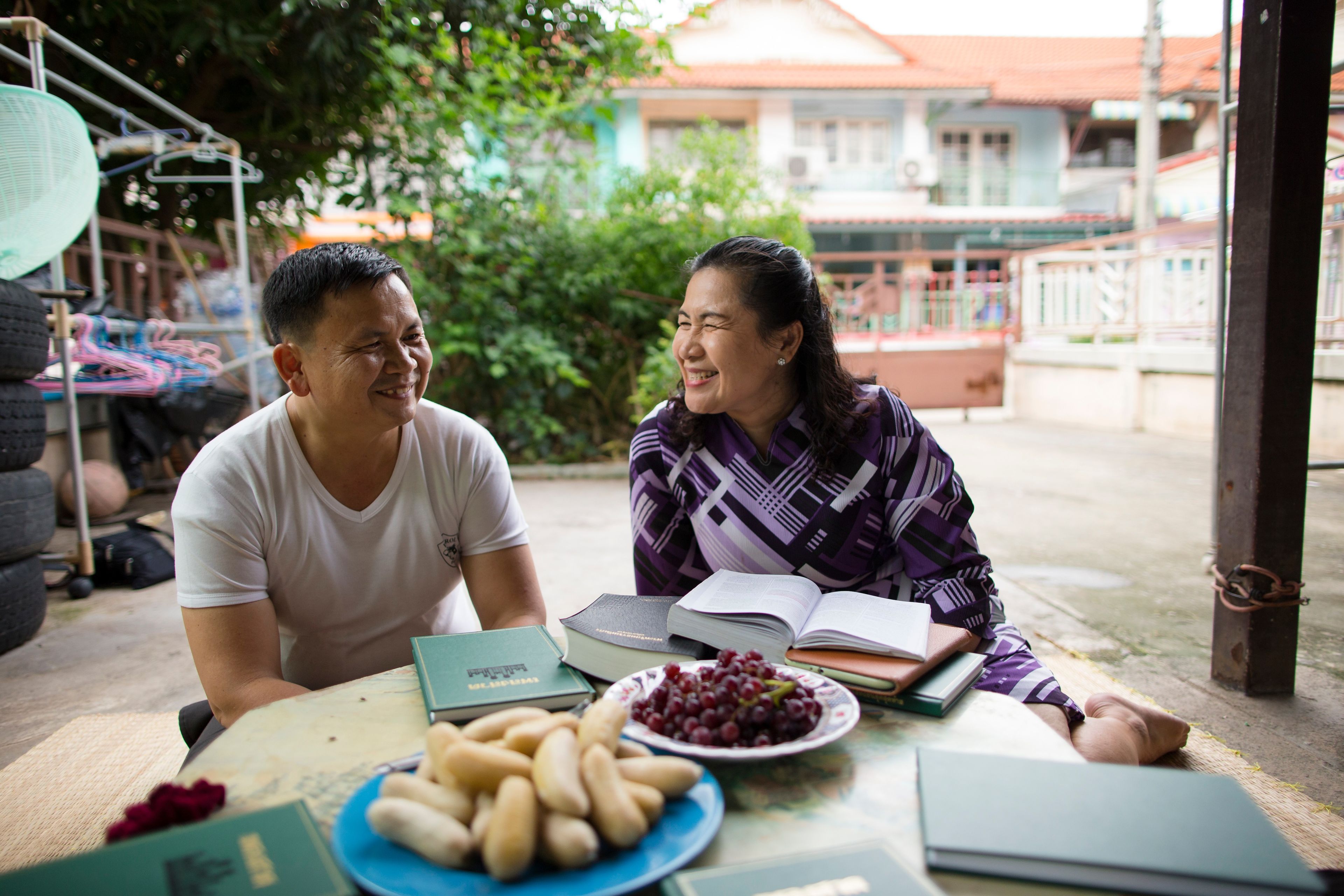 A couple from Thailand smiling and sitting at a table with gospel books.  