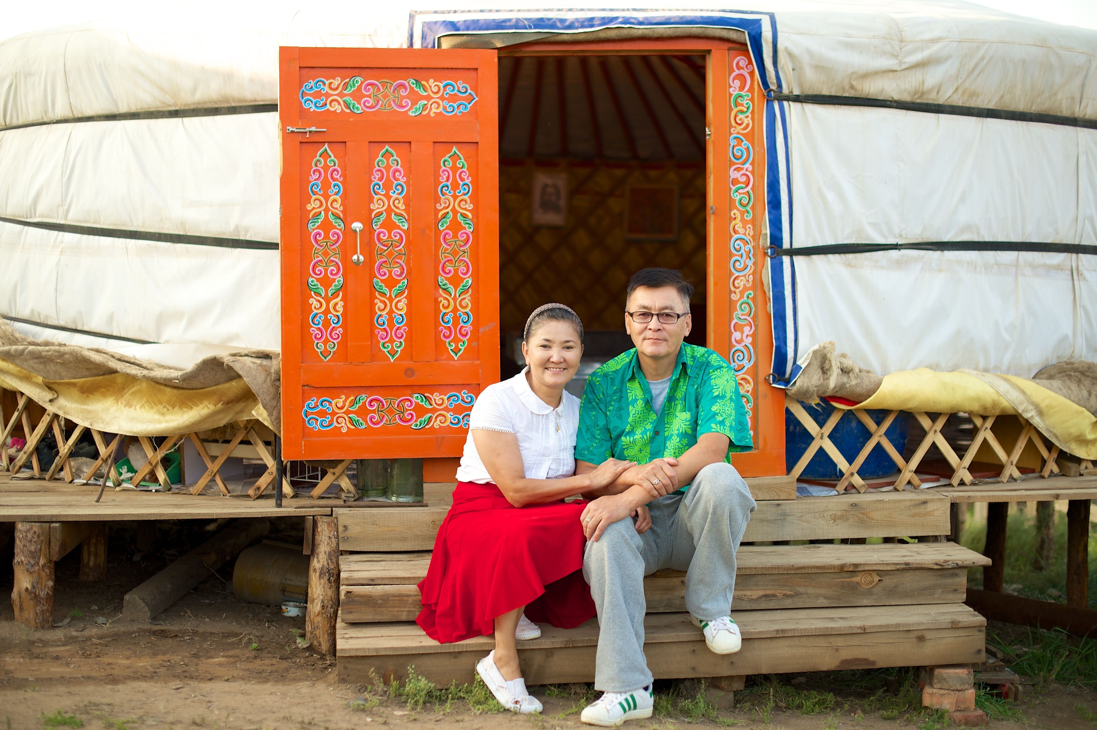 A couple from Mongolia sits on stairs by an orange door that is open.  