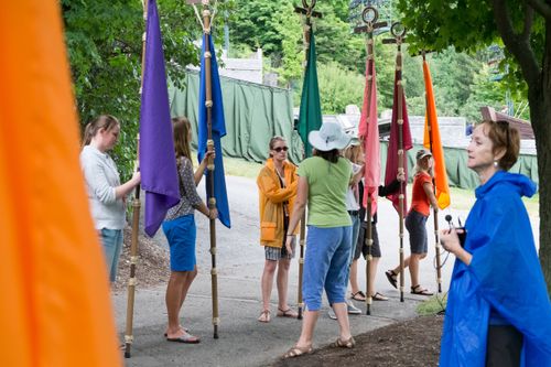 Young women from the Hill Cumorah Pageant line up holding flags on poles in a variety of colors, with two women directing them during rehearsal.