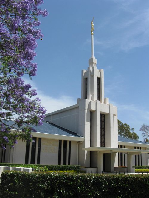 A partial view of the front of the Sydney Australia Temple, with the grounds, including bushes and a purple flowering tree.