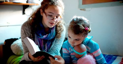 young woman reading scriptures with younger sister