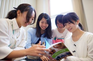 Young women are looking at their "My Family" booklets in Japan.