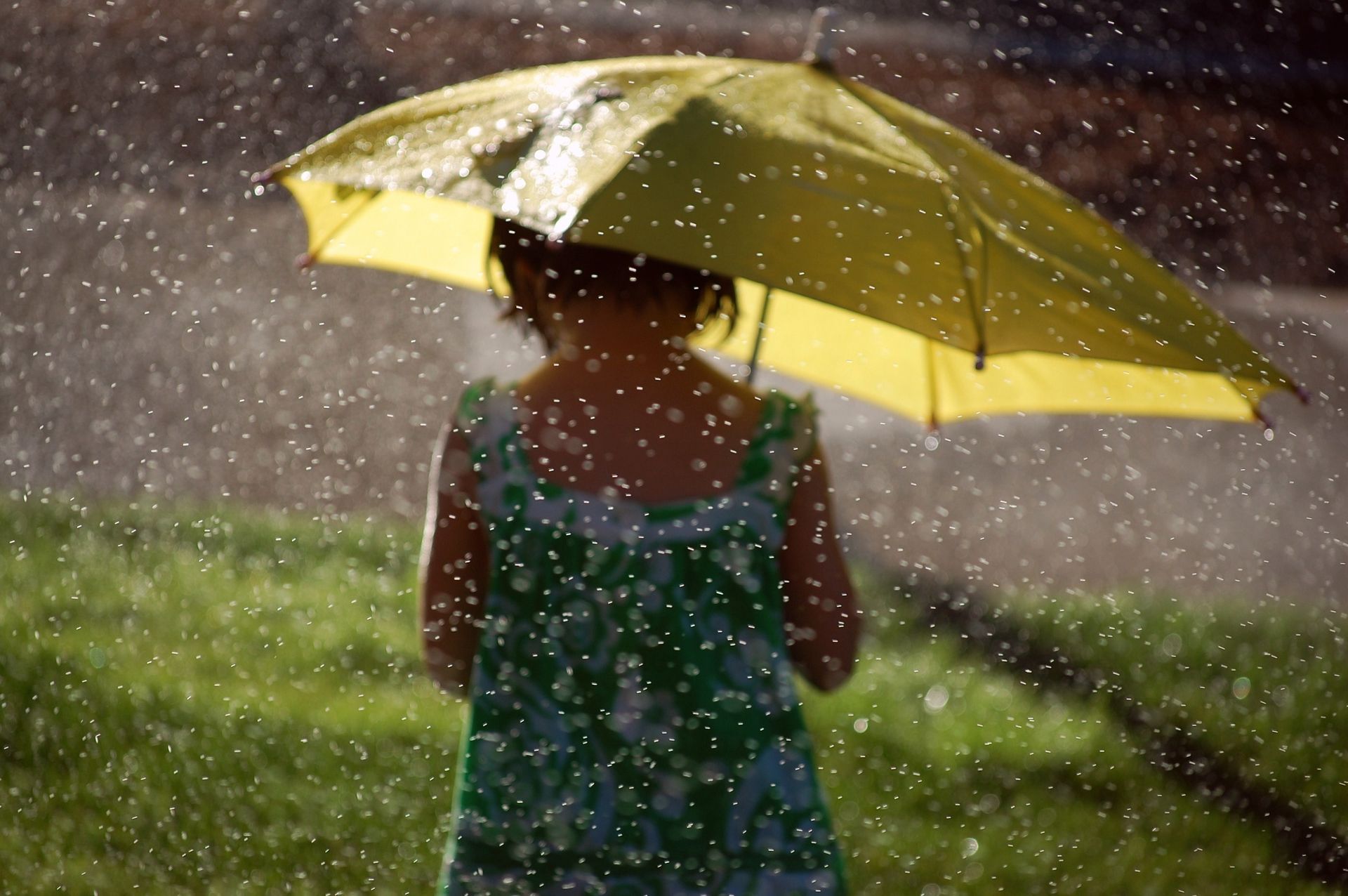 A little girl holds a yellow umbrella in the rain.