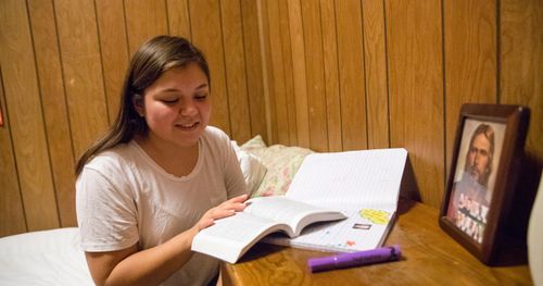 A young woman sits on her bed and reads her scriptures in her bedroom.