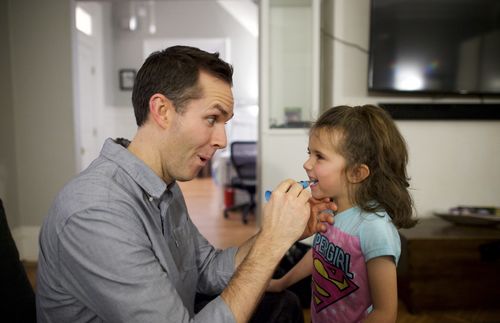 A father brushes his daughter's teeth.