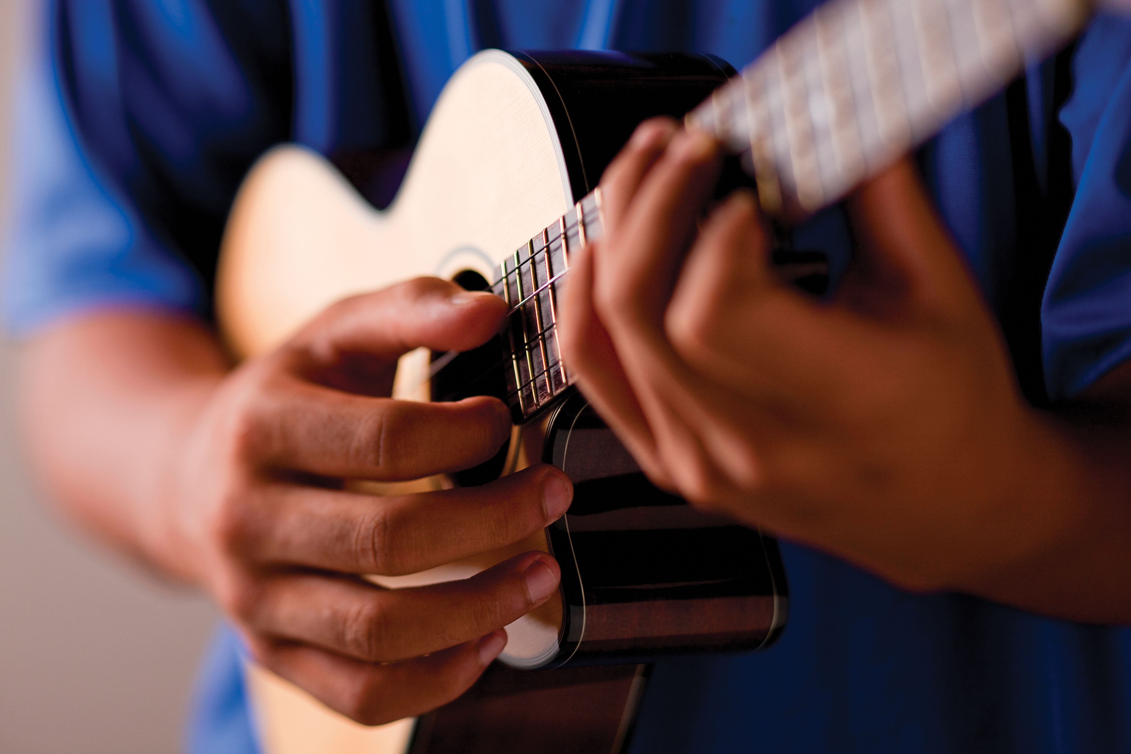 Two hands are seen strumming a ukulele.