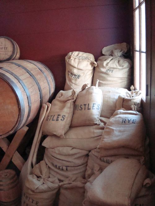 White sacks labeled “Corn,” “Rye,” etc. stacked in a corner against a red wall.