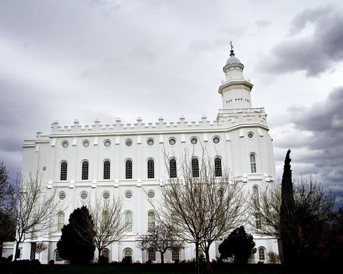 The side of the St. George Utah Temple, with a view of the windows, the spire, and the surrounding grounds, including trees.