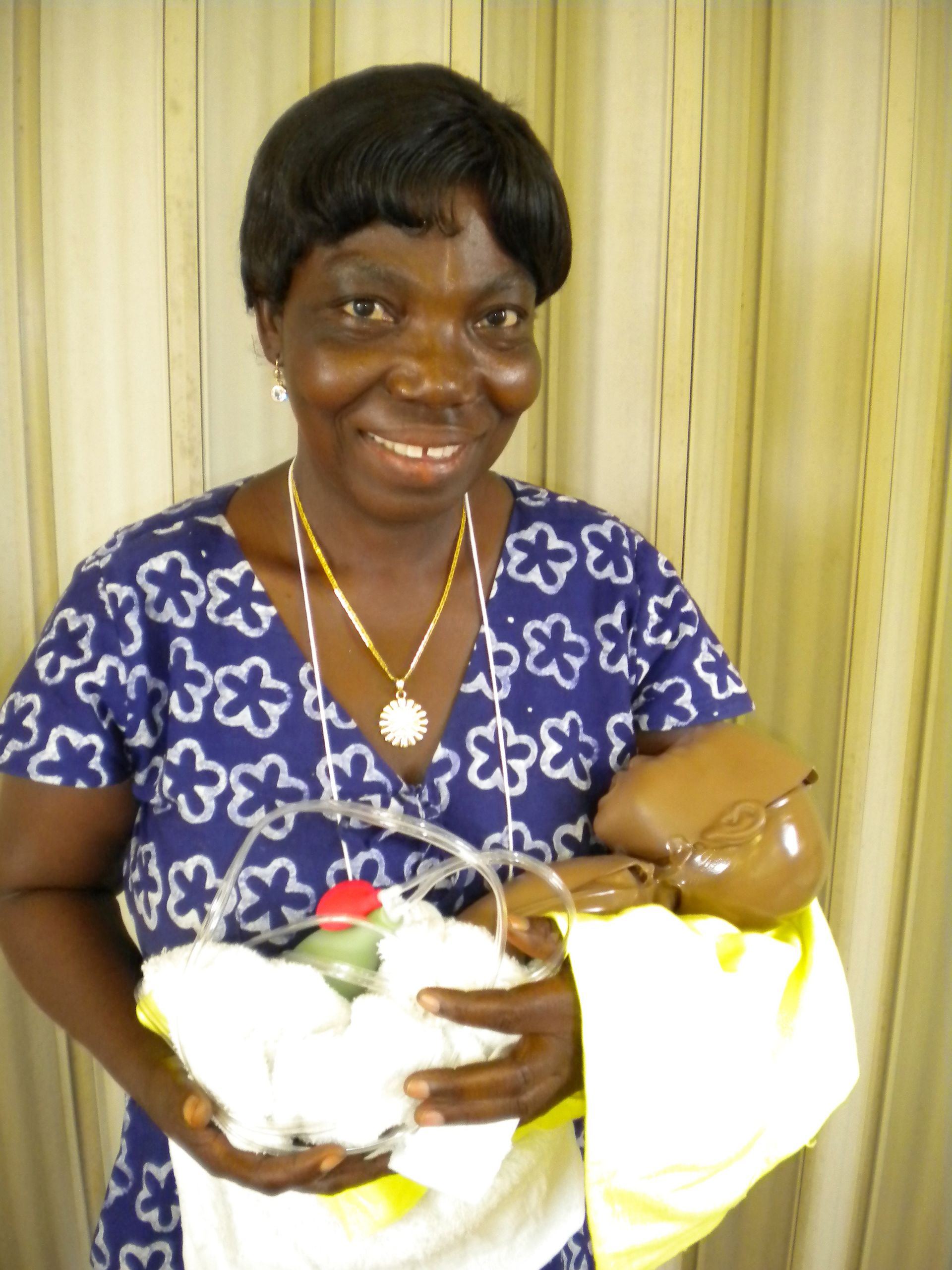 A midwife in Ghana standing and holding a CPR practice baby wrapped in a blanket.