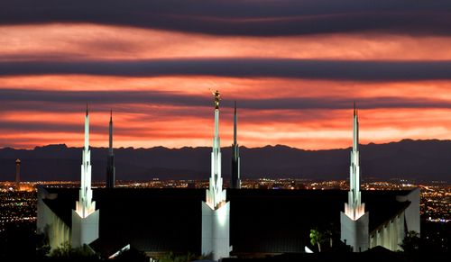 A view of the Las Vegas Nevada Temple illuminated in the evening, with an orange sky in the background and the city lights in the distance.