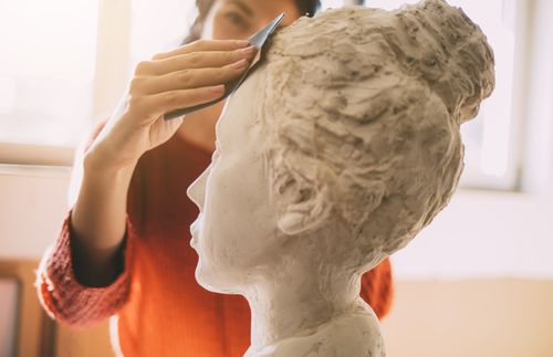 young woman sculpting a young woman’s head with clay