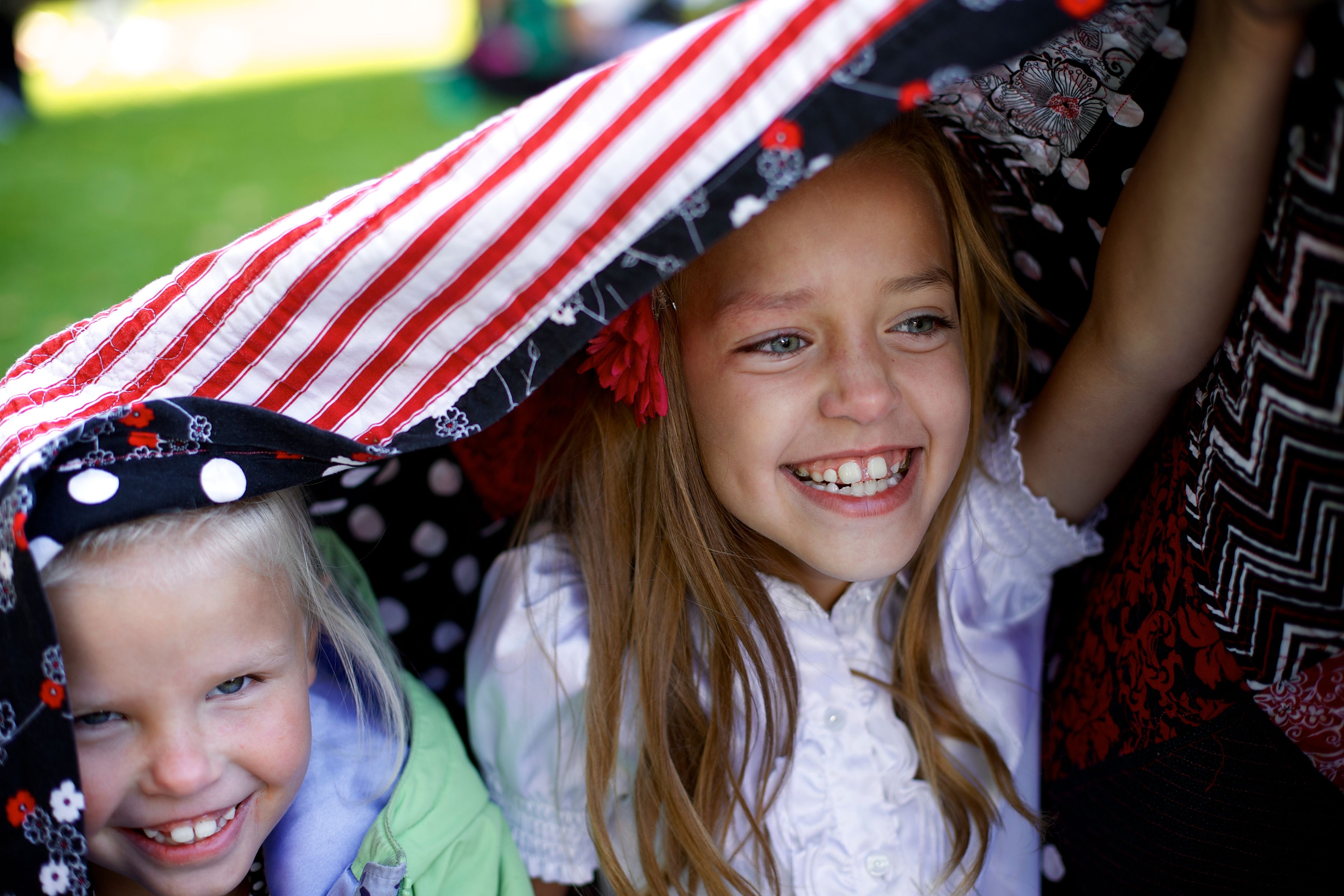 Two little girls smiling and holding a blanket over their heads outside the Conference Center.  