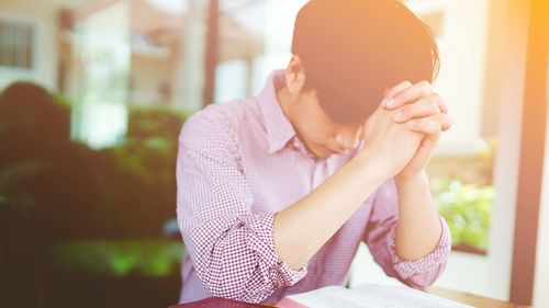 teenager praying next to open scriptures