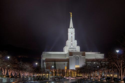 The Bountiful Utah Temple lit up on a winter’s night, with bare trees on the temple grounds.