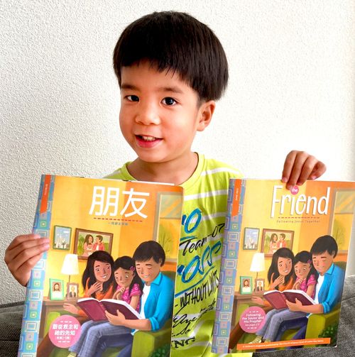 Ein Junge hält Exemplare der Zeitschrift „Unser Freund“ auf Englisch und Chinesisch in der Hand