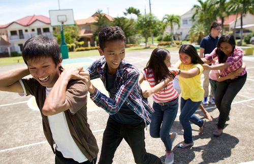 Youth in the Philippines are walking in a line and laughing and holding hands.