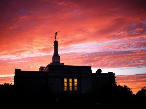 A silhouetted photograph of the Halifax Nova Scotia Temple at sunset, with a red sky behind it and a window glowing yellow from within.