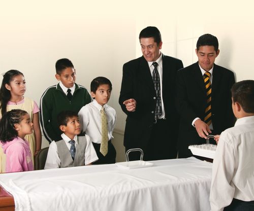 A Primary class gathered as a group at the sacrament table learning about the sacrament.