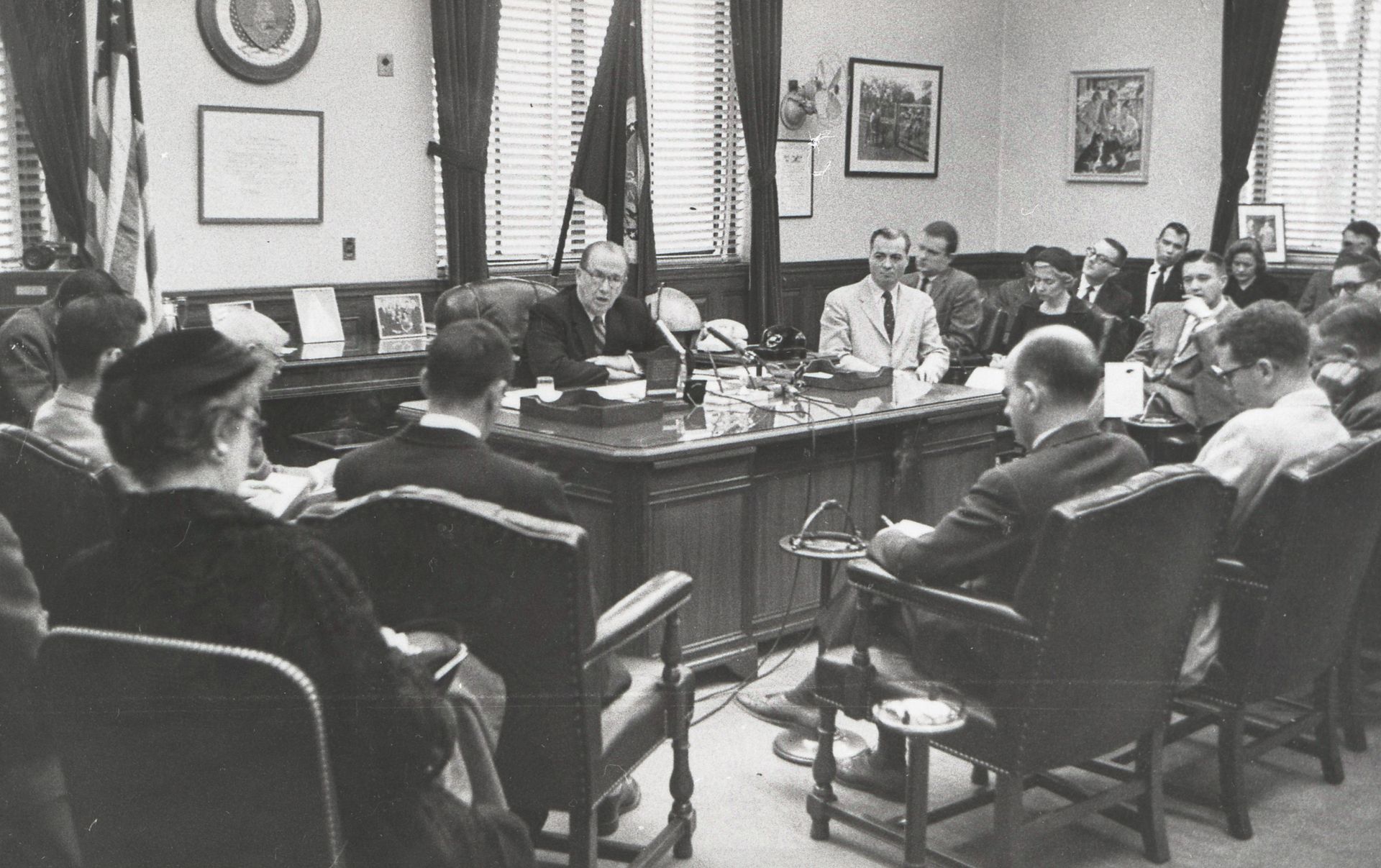 President Benson sitting behind a desk and speaking to a group of men and women.