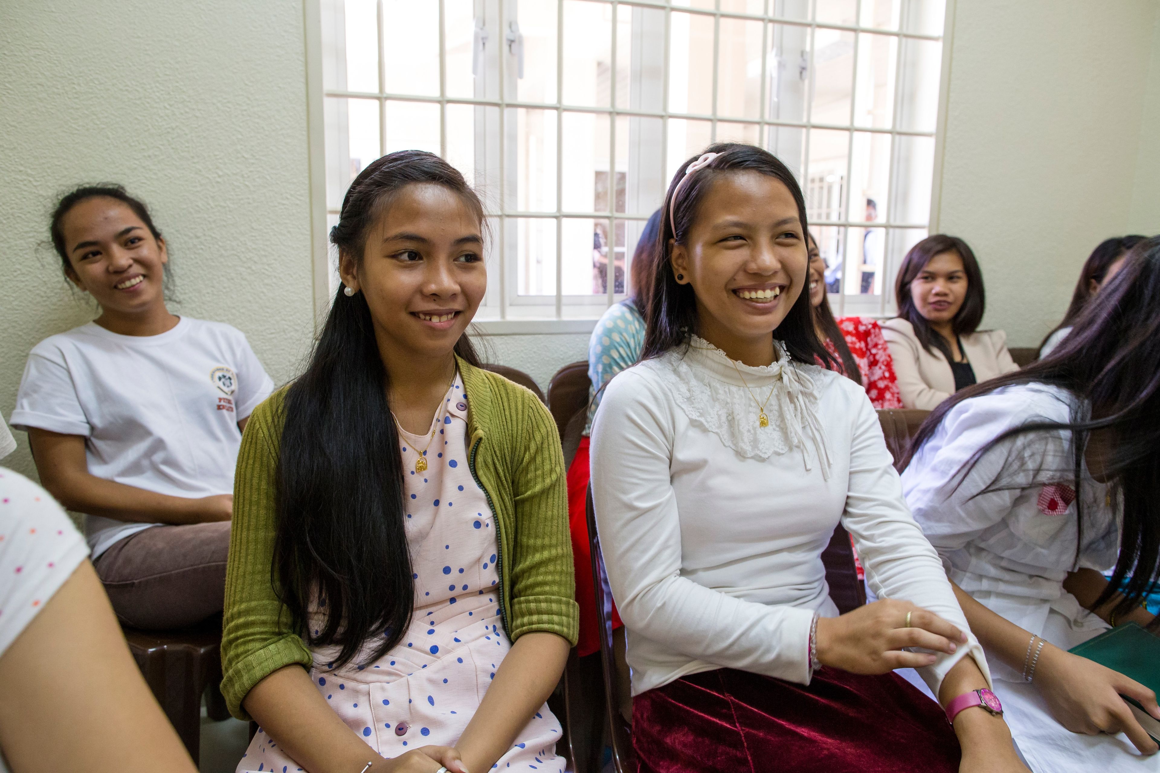 A group of young women in the Philippines sits in class together and smile.  