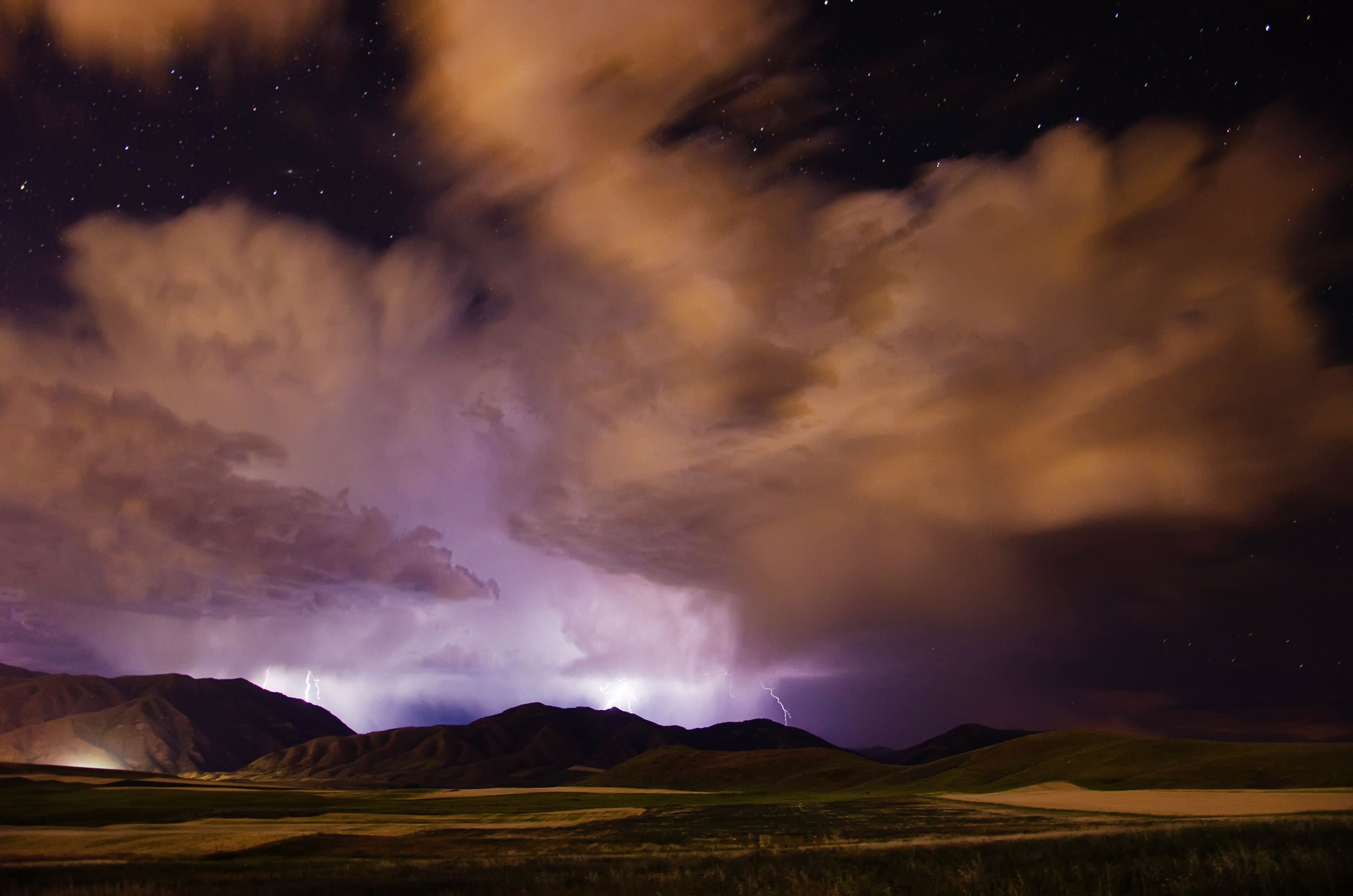 Lightning striking over a mountain range surrounded by large storm clouds at night.