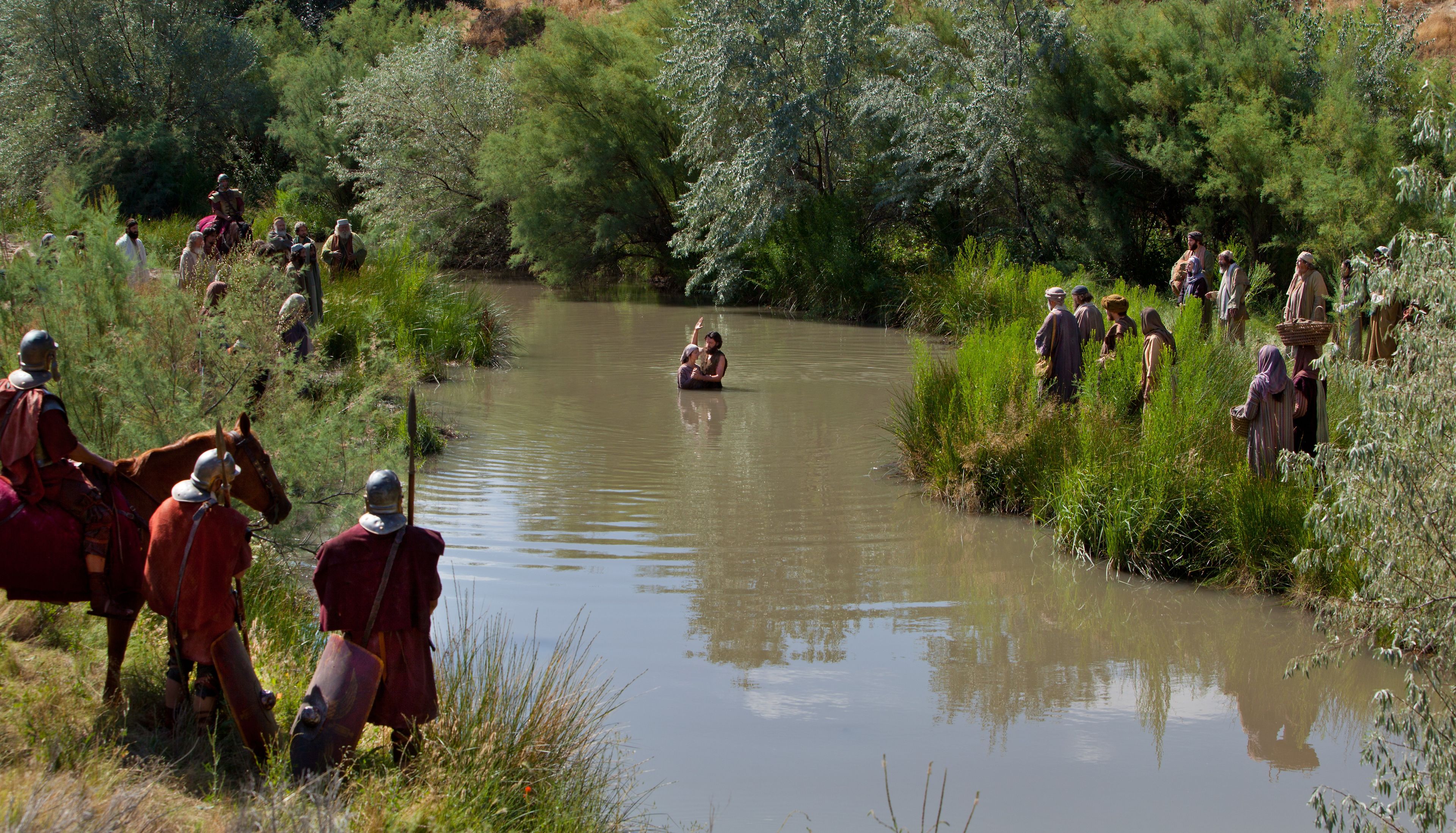 John baptizes men and women in the River Jordan.