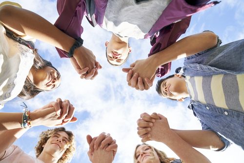 A group of young men and young women hold each other's hands in a circle and smile at each other to encourage one another.