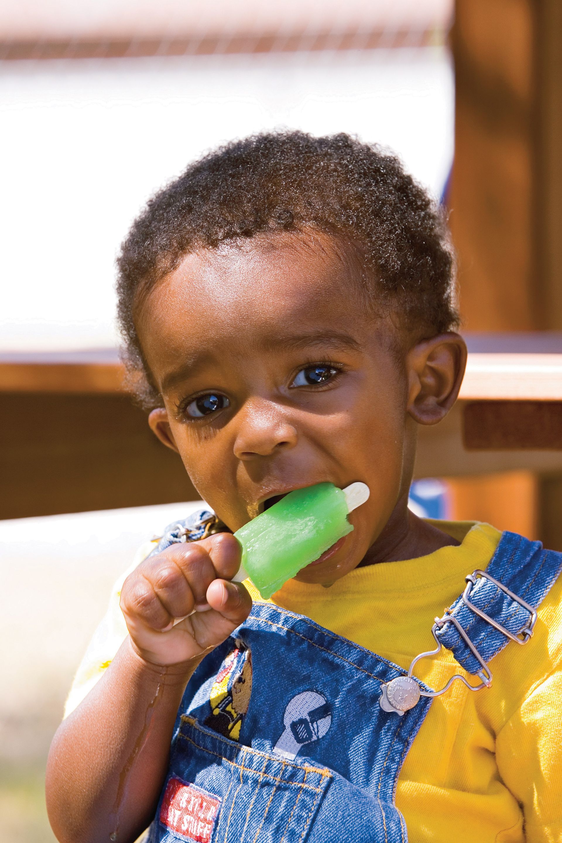 A little boy eats a green Popsicle.