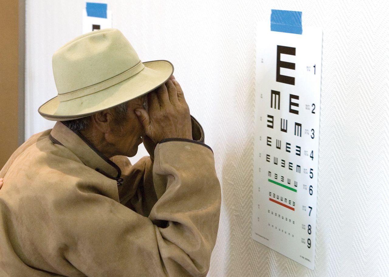A Mongolian man standing close to an eye chart to check his eyesight prior to his cataract surgery.