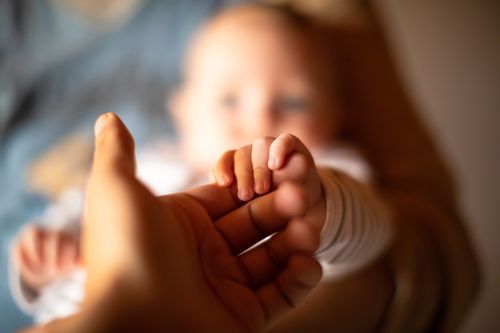 baby holding on to the finger of an adult