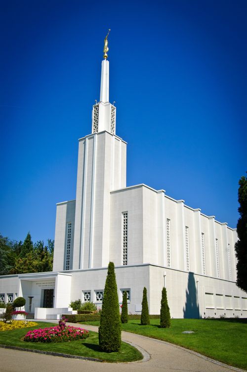 The front of the Bern Switzerland Temple on a sunny day, with well-manicured trees, bushes, and lawns.