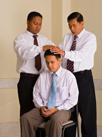 man being blessed by two men