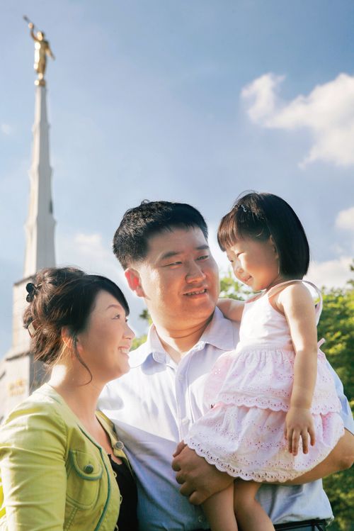 A Korean couple standing in front of the Seoul Korea Temple.  The father is holding their young daughter.