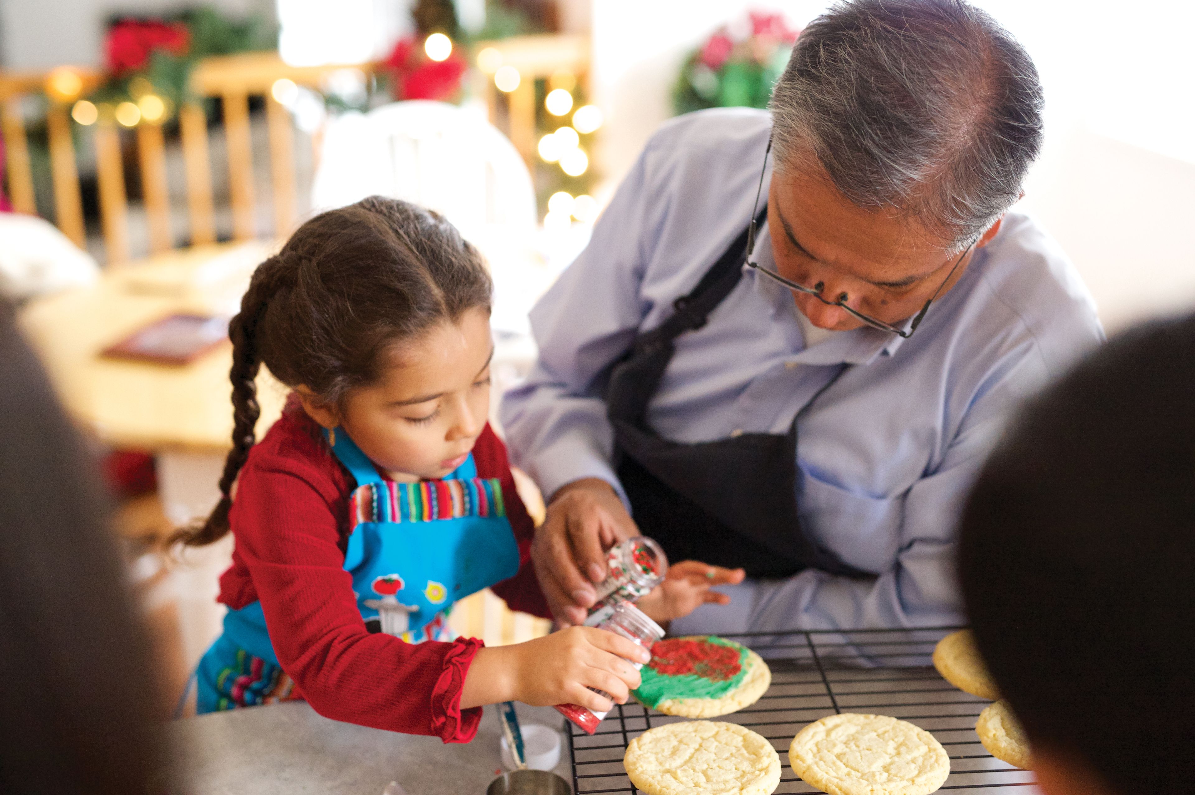 A grandfather decorates Christmas sugar cookies with his granddaughter.