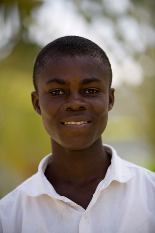 A portrait of a young man from Africa in a white buttoned shirt, standing outside.