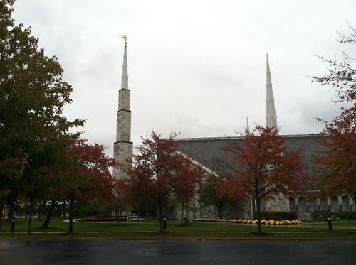 The spires on the Chicago Illinois Temple during the autumn, with red and orange leaves on the trees in the foreground.