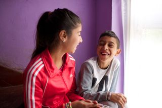 A brother and sister in Romania are sitting together on some stairs studying.