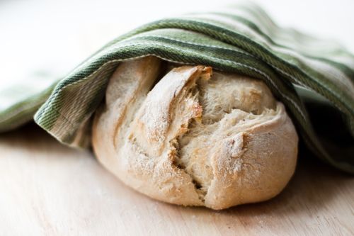 A fresh loaf of bread under a tea towel.