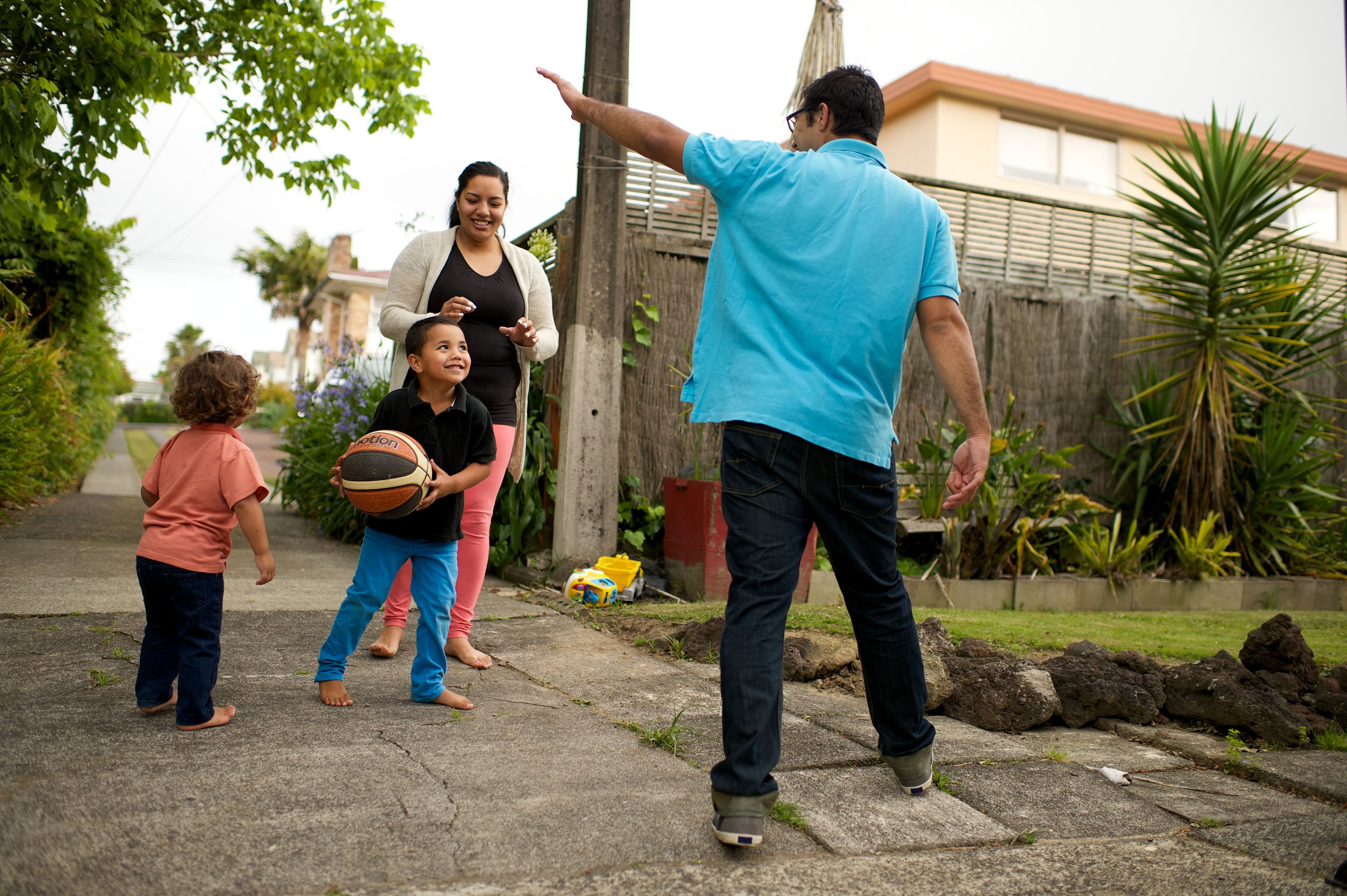 A mother and father play basketball with their two young children.