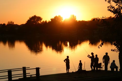 A silhouette image of a family fishing together at sunset.