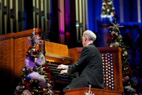A man in a black suit playing an organ next to decorated Christmas trees in the 2011 Christmas concert in the Conference Center.