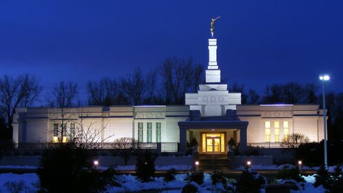 The entire St. Paul Minnesota Temple all lit up at night during the winter, with a view to the entrance. Snow is on the ground around the temple.