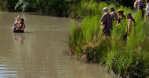 John the Baptist and a woman standing in the river Jordan with a group of people watching in the foreground. Outtakes include John the Baptist helping a woman into the water, and various scenes from a distance and close up.