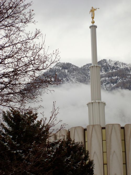The spire of the Provo Utah Temple seen in front of a fog-covered mountain in the background.