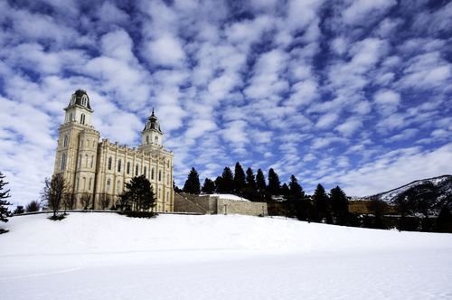 A view of the Manti Utah Temple and grounds covered in snow in winter, with a blue sky and clouds overhead.