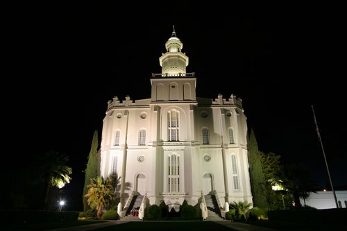 A view up the front of the St. George Utah Temple, including the two staircases and two doors, all lit up at night.