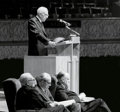President Joseph Fielding Smith standing at the pulpit and speaking at the Manchester area conference in 1971, with three General Authorities sitting nearby.