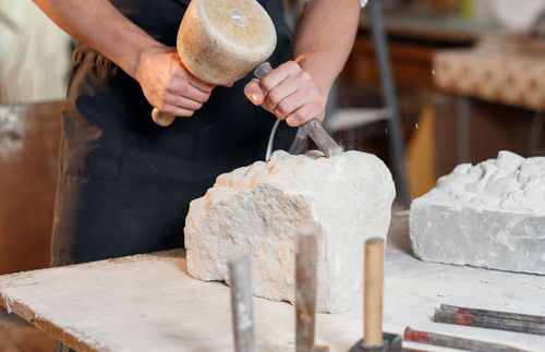 hands using a hammer and chisel to carve a stone
